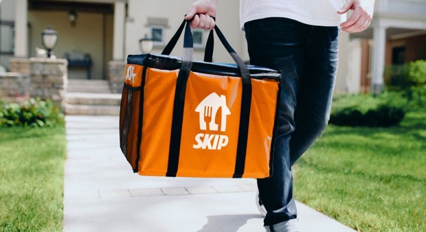 A Skip courier carrying an orange Skip delivery bag up a front walkway